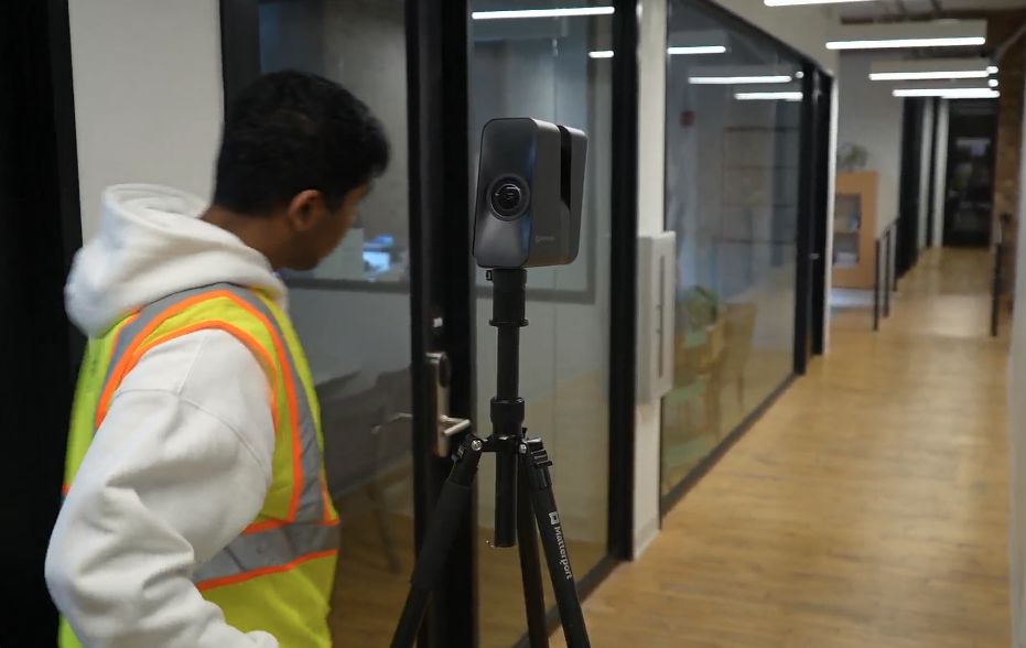 A worker sets up a tripod-mounted scanner in an office corridor